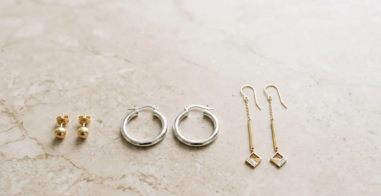 Coleccion minimalista de tres pares de pendientes sobre superficie de marmol beige representando versatilidad para diferentes tipos de citas