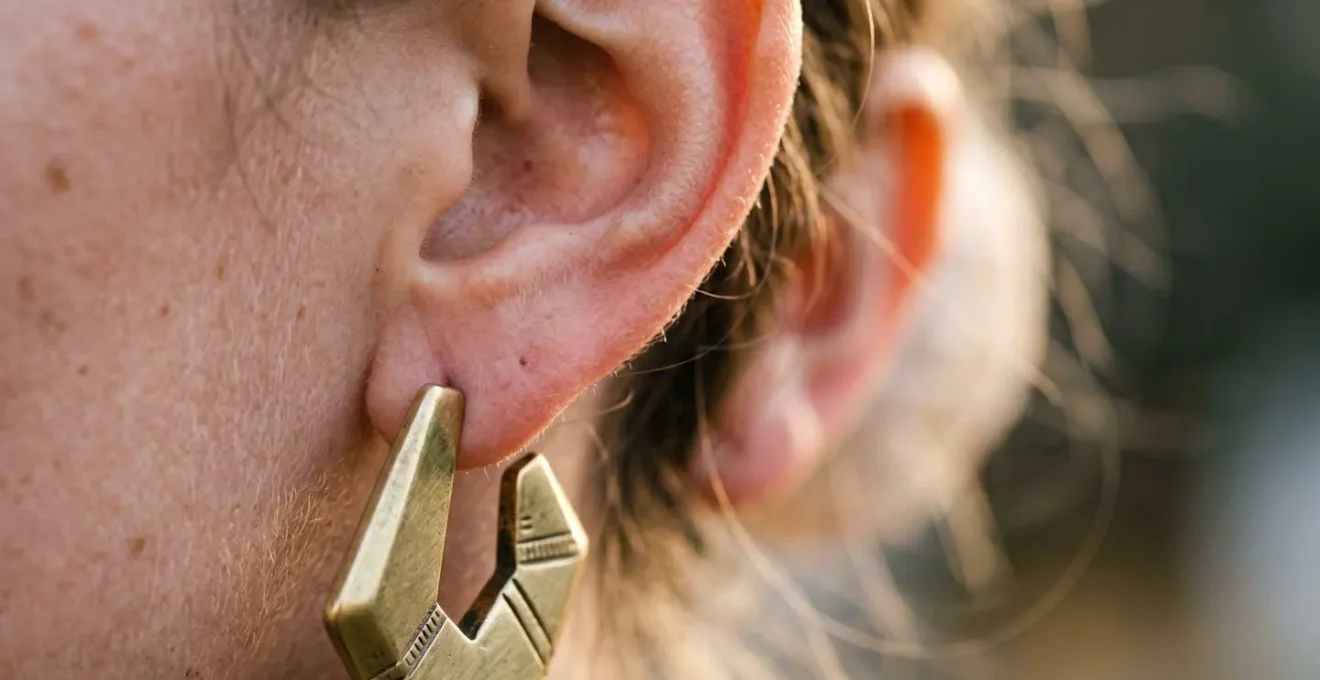 Detalle macro de oreja con un solo pendiente asimétrico geométrico dorado